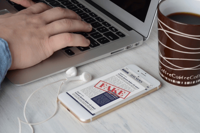 Liikemies näppäimistöllä, kuppi kahvia ja digitaalisia väärennöksiä älypuhelimessa
